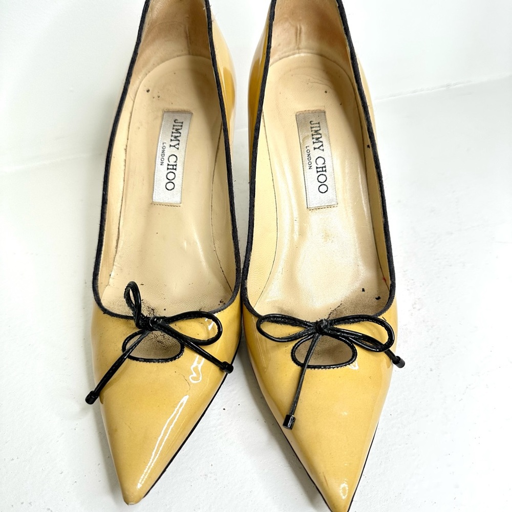 Jimmy choo patent leather tan pumps with black bow center and black piping.